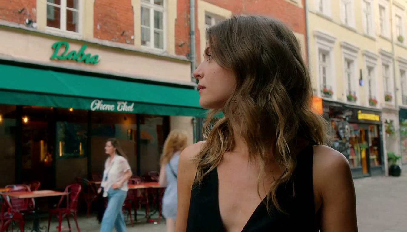 MiniMax H3 AI video example showing a woman with wavy hair wearing a black top stands on a city street, looking to the side